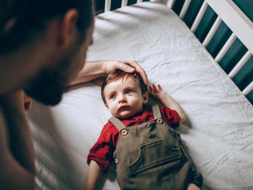 Vater streichelt seinen kleinen Sohn im Kinderbett