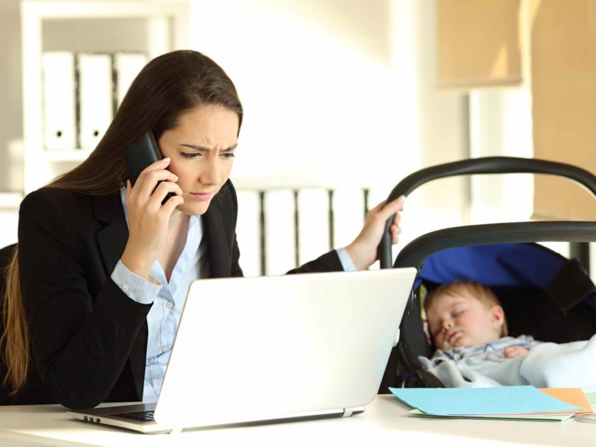 Junge berufstätige Frau arbeitet am PC und betreut parallel ihr Baby