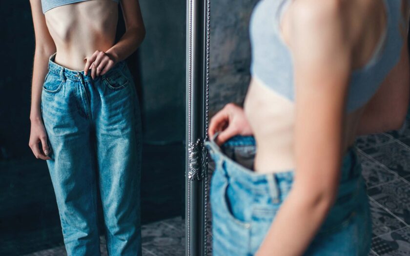 extrem dünnes Mädchen betrachtet sich vor einem Spiegel