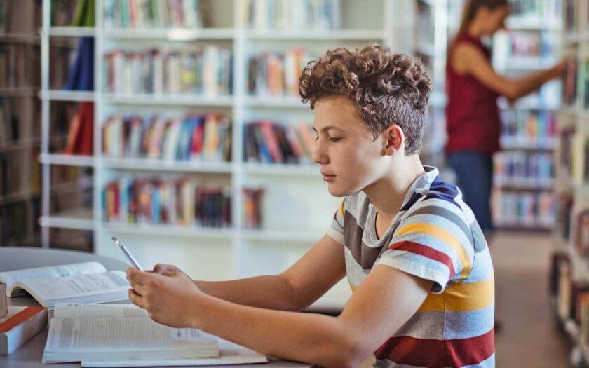 Schüler in einer Bücherei lernt mit dem Smartphone