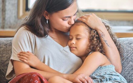Alleinerziehende Mutter sitzt mit ihrem KInd auf dem Sofa und liebkost es